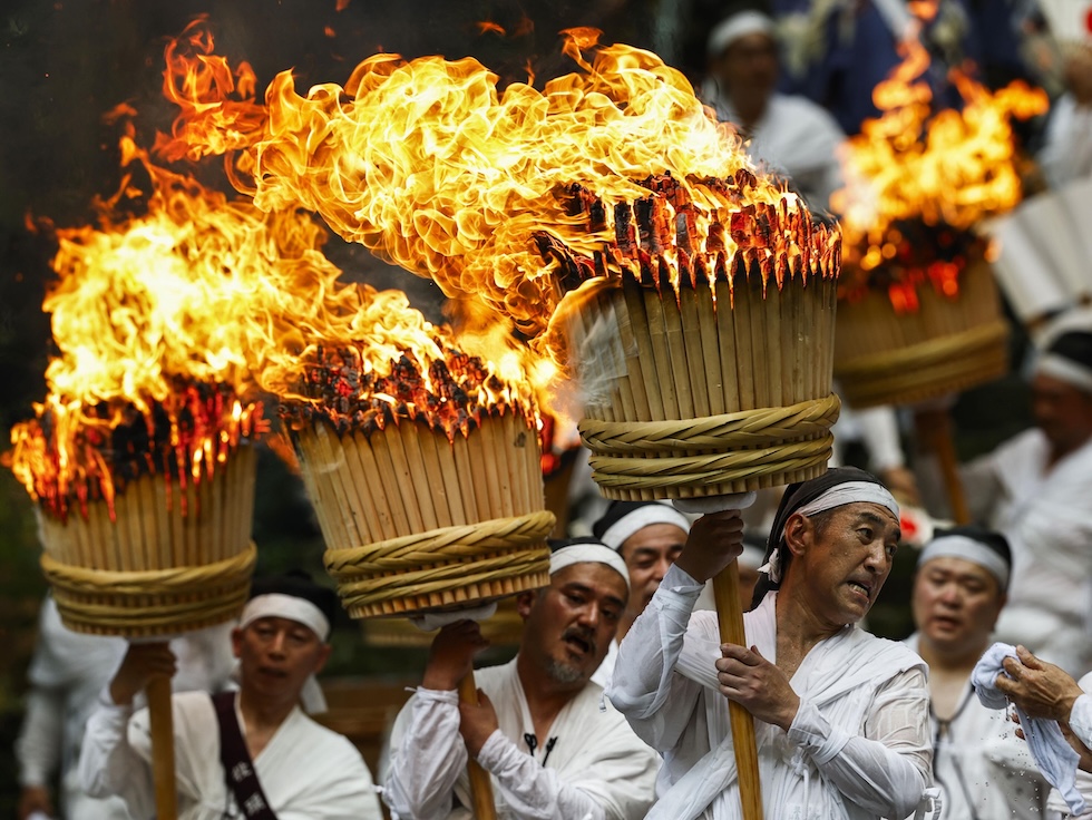 Alcuni uomini sfilano con torce infuocate durante un festival (Kyodo News via AP)