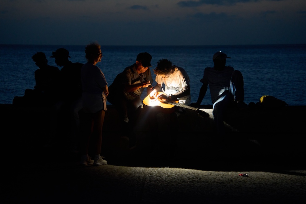 Un uomo cambia la corda di una chitarra alla luce di una torcia sul lungomare del Malecón, durante uno dei numerosi blackout generalizzati sull'isola (AP Photo/Ramon Espinosa)