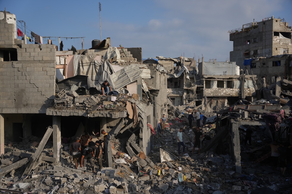 Persone palestinesi raccolgono i propri effetti personali tra le macerie degli edifici distrutti da un bombardamento israeliano (AP/Abdel Kareem Hana)