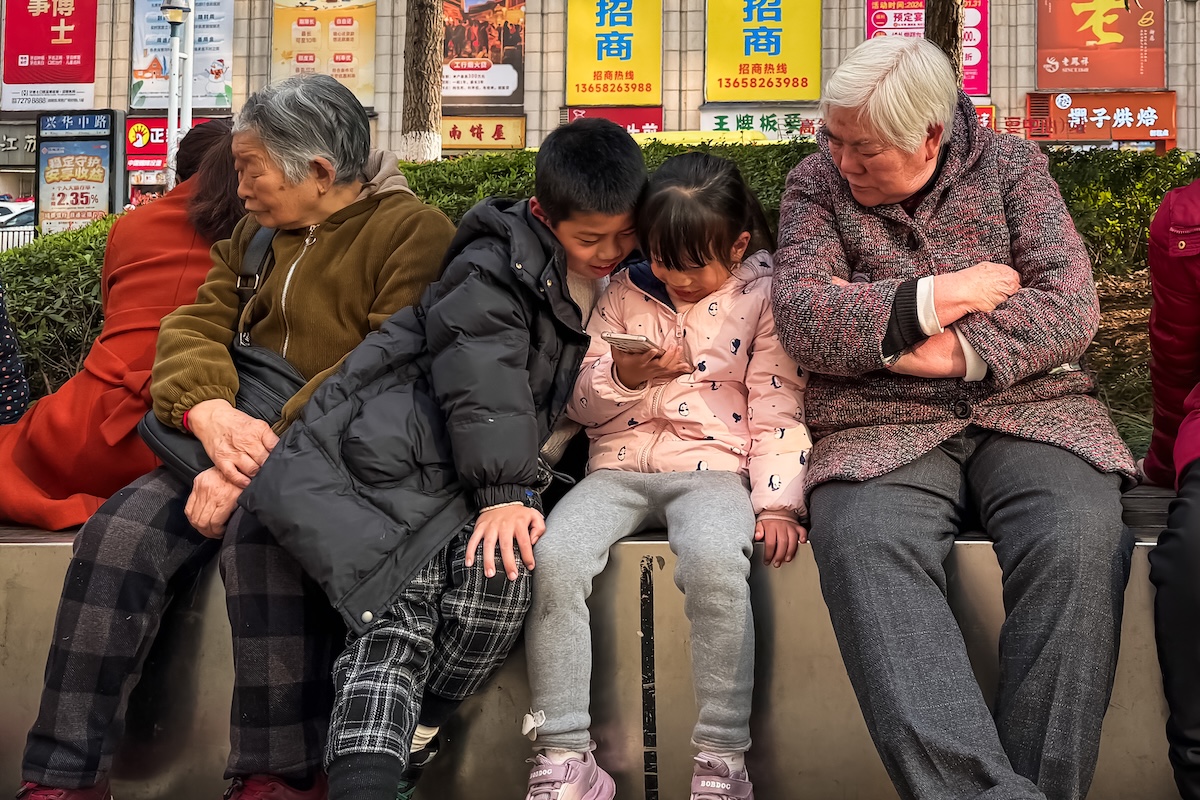 Due bambini con uno smartphone seduti vicino a due donne anziane