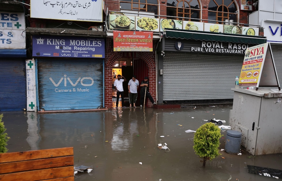 Persone fuori dai negozi tra l'acqua alta, dopo le forti piogge che hanno causato allagamenti in diverse zone della città (EPA/FAROOQ KHAN/ansa)
