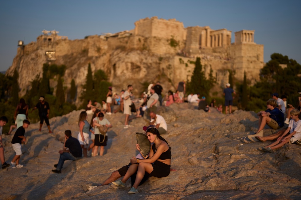 Una turista si rinfresca con un ventaglio, seduta sulla collina dell’Areòpago tra gli altri visitatori, con l’Acropoli sullo sfondo (AP Photo/Petros Giannakouris)
