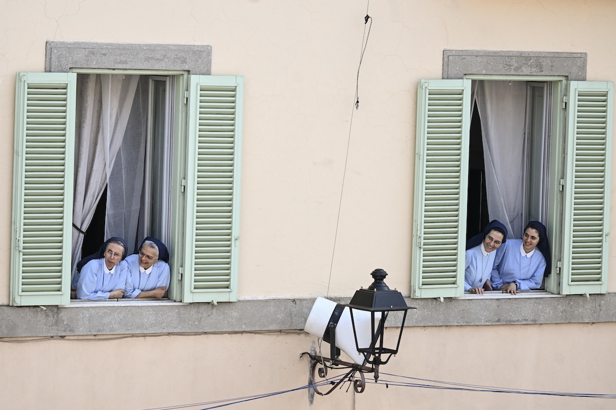 Quattro suore assistono alla preghiera dell’Angelus dall’ingresso del Palazzo Apostolico affacciato su Piazza della Libertà, presso la residenza estiva papale di Castel Gandolfo, Roma (Riccardo Antimiani/ANSA)