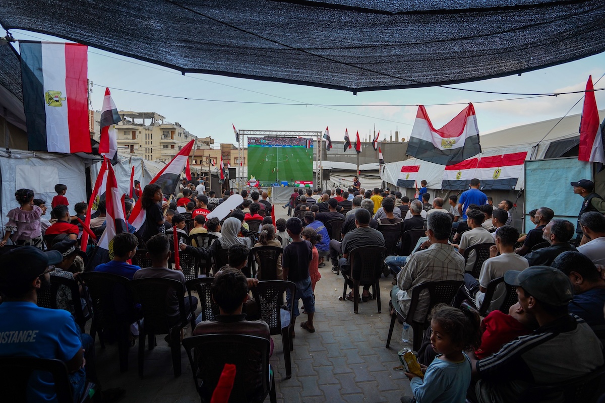Un gruppo di residenti palestinesi guarda una partita dei Mondiali proiettata su un mega schermo allestito in un campo
