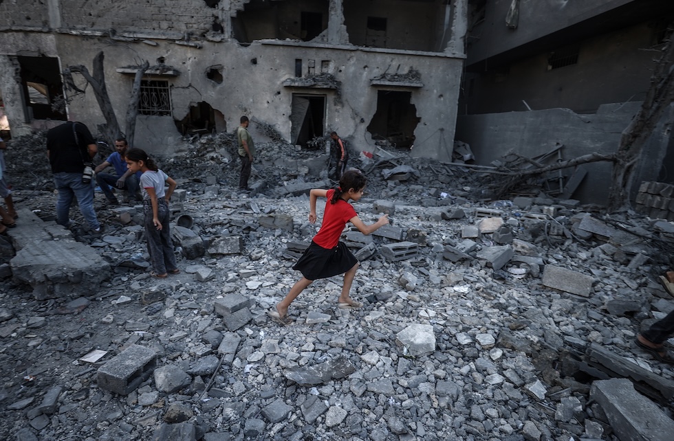 Una bambina corre tra le macerie degli edifici colpiti dai bombardamenti israeliani (Ali Jadallah/Anadolu via Getty Images)