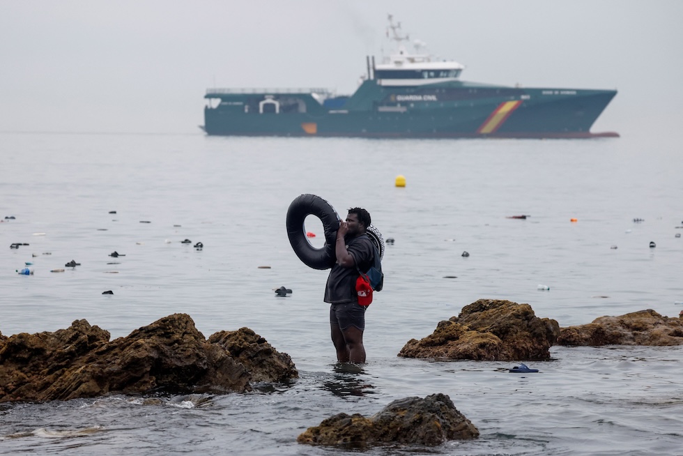 Un uomo gonfia un salvagente in acqua, mentre sullo sfondo passa una nave della Guardia Civil spagnola (REUTERS/Jon Nazca)