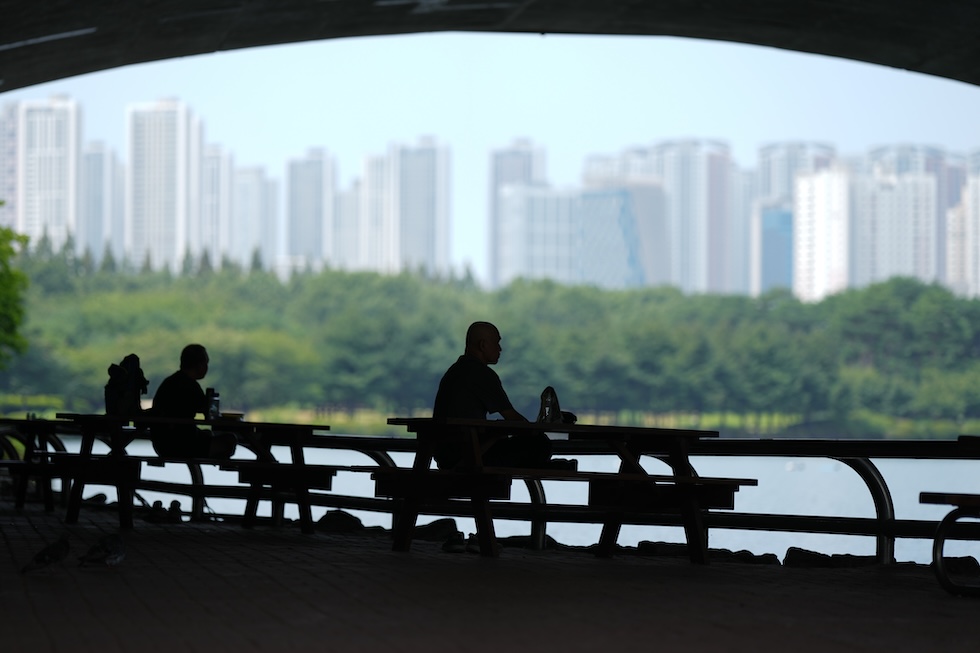 Persone sedute all'ombra, di fronte alla skyline della città (AP Photo/Lee Jin-man)