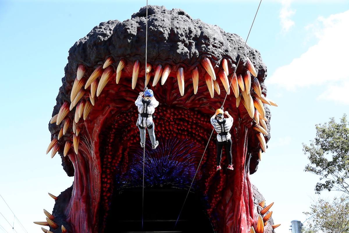 Due persone su una teleferica entrano nella bocca di un’enorme replica di Godzilla in un parco a tema