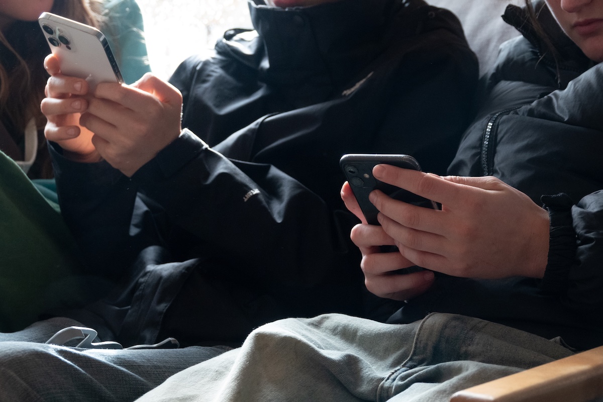 Un particolare di due ragazzi seduti mentre reggono uno smartphone