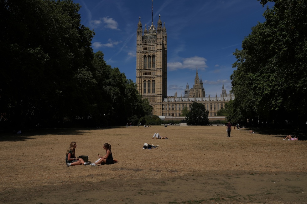 Persone su un prato, in uno dei parchi ingialliti per la siccità, vicino al palazzo di Westminster (AP Photo/Kin Cheung)