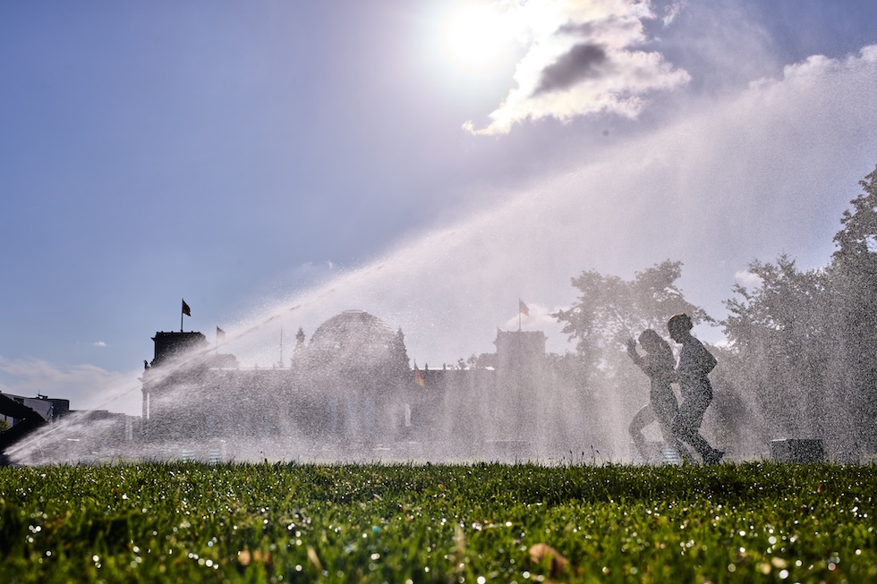 Due donne corrono davanti al palazzo del Reichstag, passando accanto ai getti d'acqua di un irrigatore (AP Photo/Markus Schreiber)