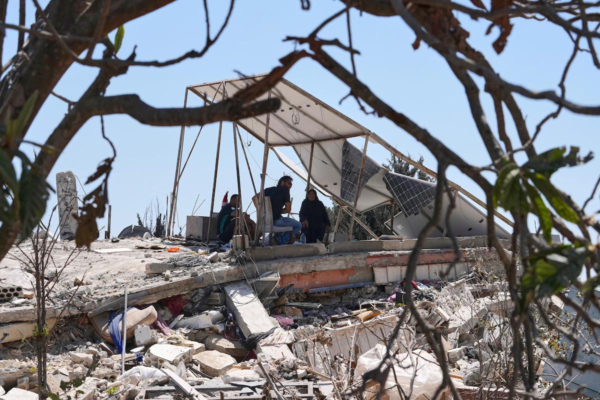 Una famiglia libanese si ripara dal sole sotto un pannello solare danneggiato dopo che la loro casa è stata distrutta a Zawtar al Gharbieh, nel sud del Libano, 5 agosto 2026 (AP Photo/Mohammed Zaatari)
