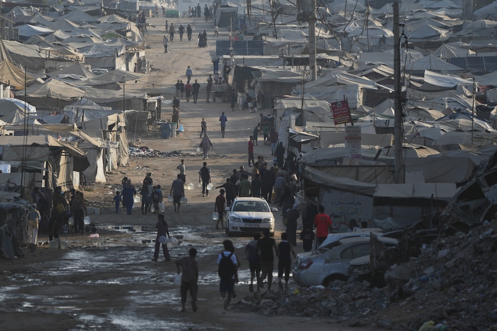 Palestinesi camminano tra le tende e le macerie degli edifici distrutti lungo la strada costiera (AP Photo/Abdel Kareem Hana)