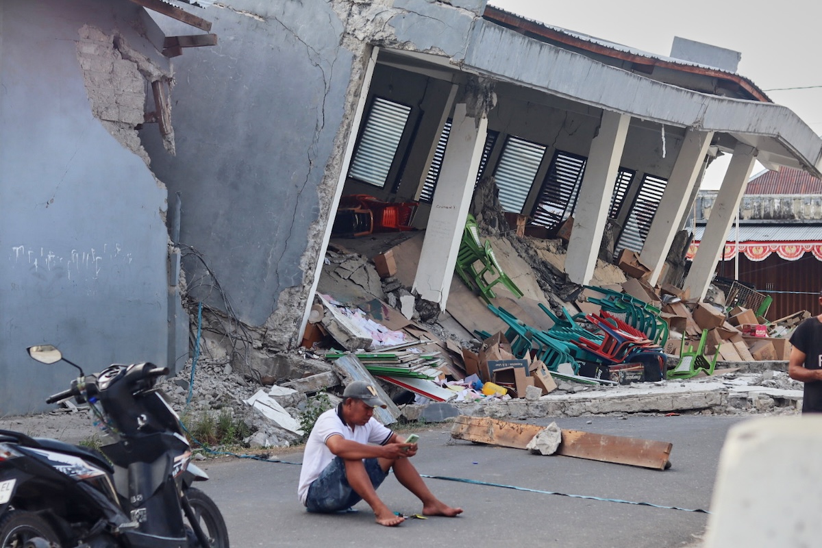 Un uomo al cellulare seduto davanti a un edificio distrutto a causa del terremoto di magnitudo 7.7 che ha provocato la morte di decine di persone (AP Photo/Aquila Handayani Abbas)