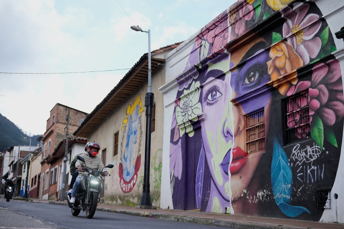 Un motociclista passa davanti a un murale nel centro di Bogotà, nel febbraio del 2026. (AP/Fernando Vergara)