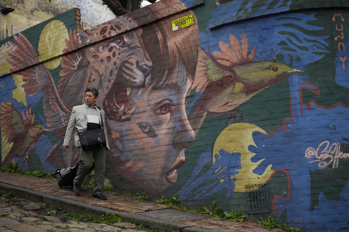 Un uomo cammina davanti a un murale nel quartiere della Candelaria, nel 2024 (AP/Fernando Vergara)