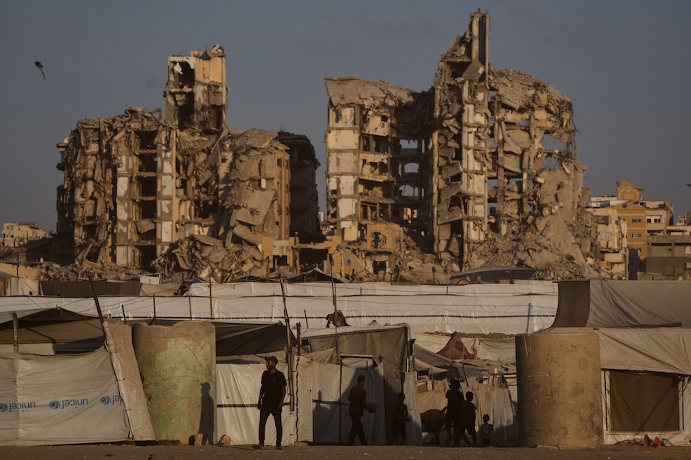 Persone tra le tende di un campo profughi palestinese, circondate dalle rovine degli edifici distrutti dai bombardamenti israeliani (AP Photo/Jehad Alshrafi)