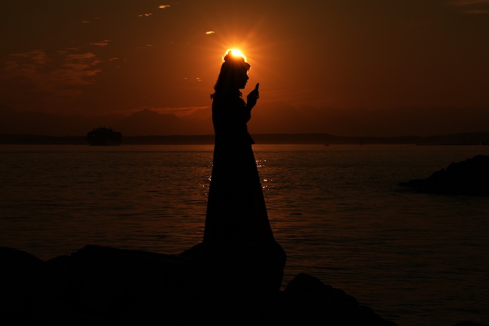 Una donna con in mano il telefono, in controluce su una spiaggia del Myrtle Edwards Park, affacciata sulla baia di Elliott (AP Photo/Lindsey Wasson)