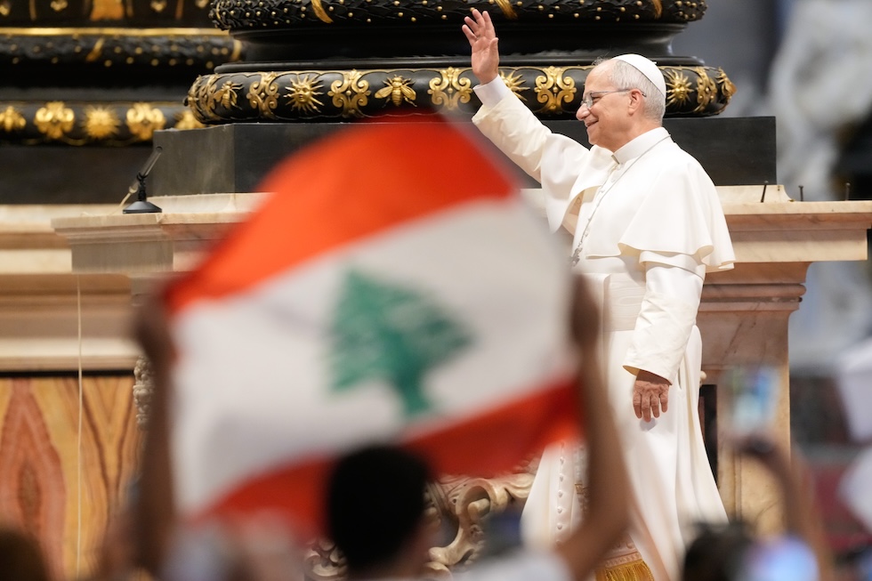 Papa Leone XIV saluta i fedeli durante l'udienza generale nella basilica di San Pietro, davanti a una bandiera del Libano (AP Photo/Gregorio Borgia)
