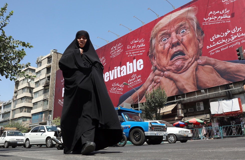 Una donna cammina per strada passando accanto a un enorme cartellone anti-Trump (EPA/ABEDIN TAHERKENAREH via Ansa)
