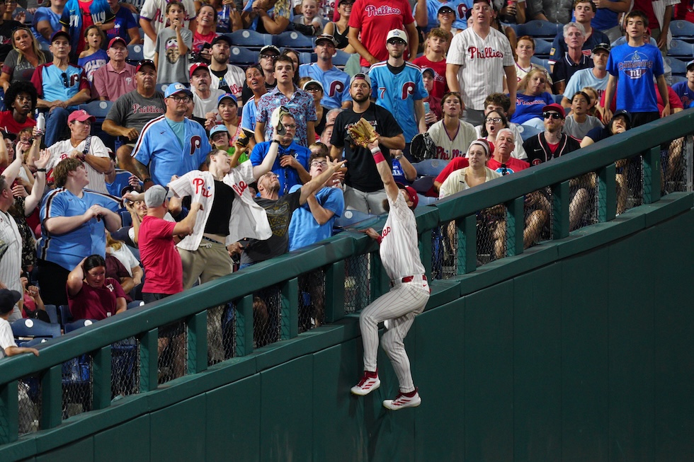 Il giocatore dei Philadelphia Phillies Brandon Marsh si arrampica sulla recinzione per cercare di prendere al volo una palla battuta in zona di foul (AP Photo/Derik Hamilton)