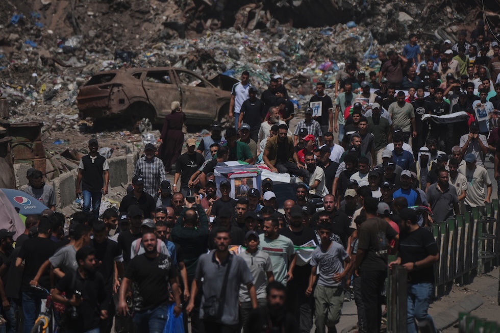 Un gruppo di persone trasporta i corpi, avvolti nelle bandiere palestinesi, di persone uccise dagli attacchi israeliani e i cui resti sono stati recentemente recuperati dalle macerie (AP Photo/Jehad Alshrafi)