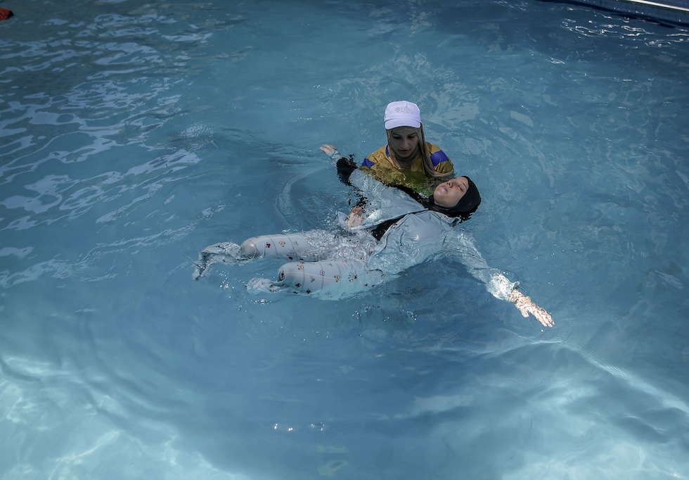 Una donna con entrambe le gambe amputate nuota in piscina dietro la supervisione di un’allenatrice (Saeed M. M. T. Jaras/Anadolu via Getty Images)
