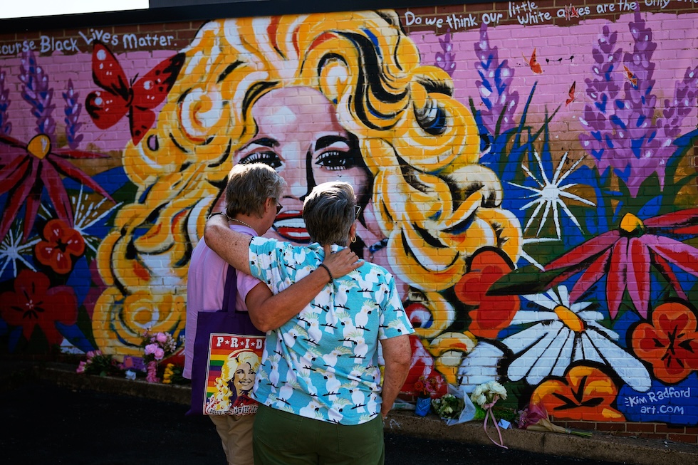 Due persone abbracciate davanti a un murale di Dolly Parton (AP Photo/Chris Pizzello)