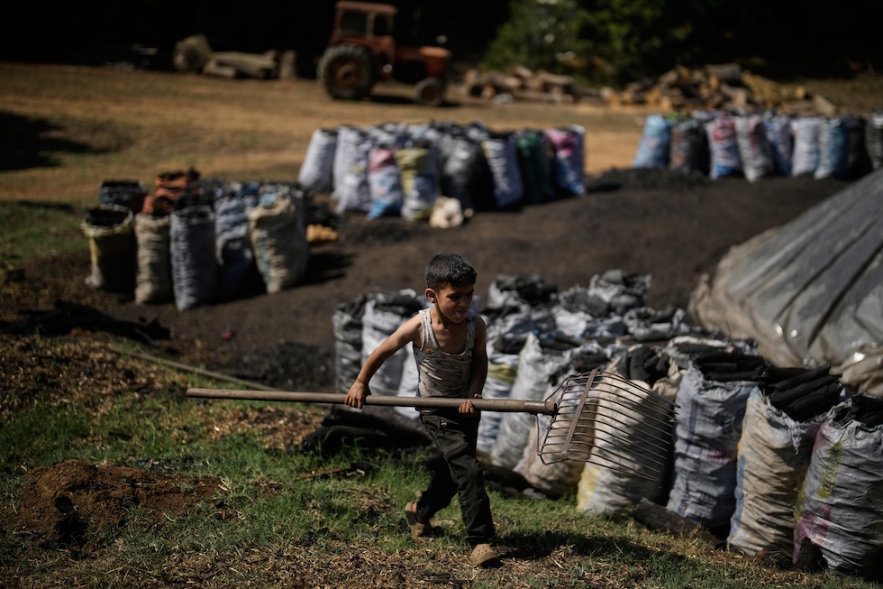 Un bambino porta un rastrello per aiutare il padre a lavorare alle fornaci per la produzione di carbone vegetale (AP Photo/Khalil Hamra)

