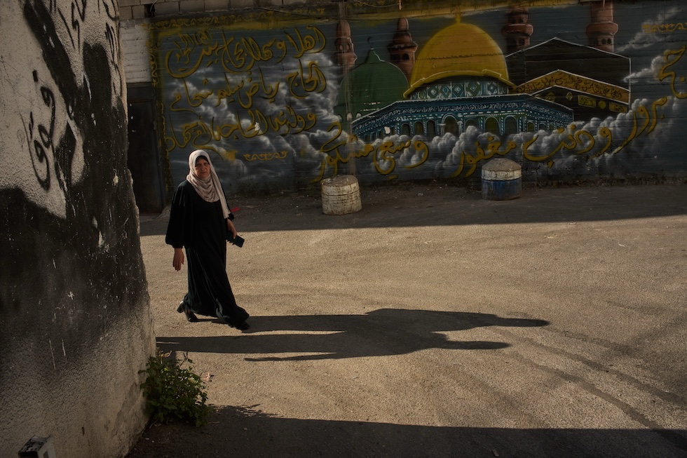 Una donna palestinese cammina vicino a un murale della Cupola della Roccia di Gerusalemme e della Kaaba, il luogo più sacro dell’Islam
(AP Photo/Leo Correa)