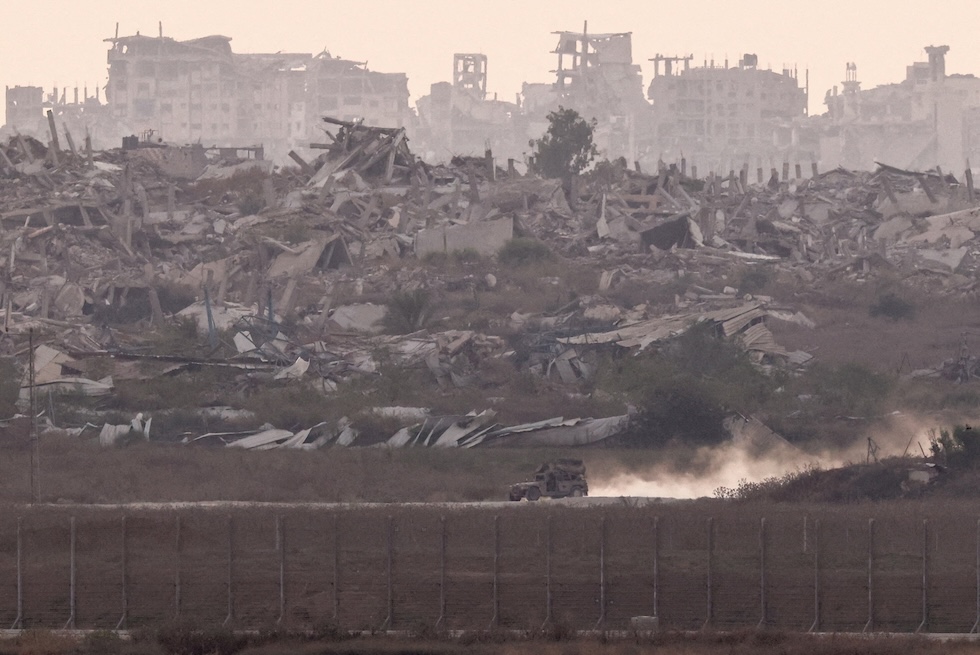 Un veicolo militare israeliano passa davanti alle macerie, fotografato dal lato israeliano del confine (REUTERS/Amir Cohen)