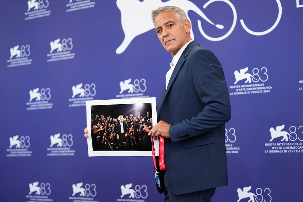 L'attore George Clooney tiene in mano una fotografia scattata alla Mostra del cinema di Venezia nel 2025 e consegnatagli dai fotografi durante il photocall di quest’anno (Scott A Garfitt/Invision/AP)