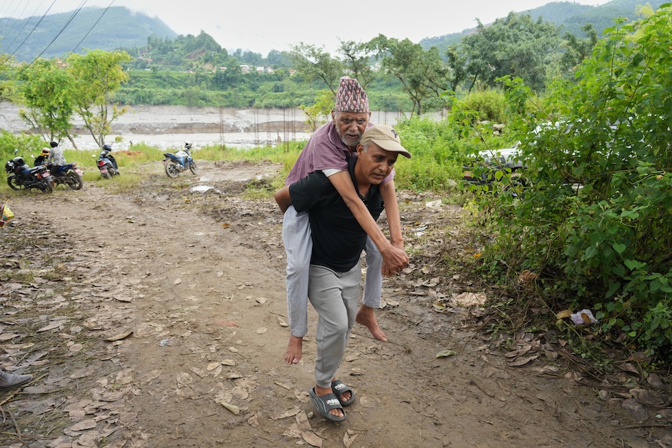 Un uomo di 86 anni portato in spalleadal figlio dopo essere stato trasportato su una teleferica costruita per far attraversare il fiume Trishuli ai cittadini rimasti bloccati a seguito delle esondazioni (AP Photo/Rajesh Kumar Singh)