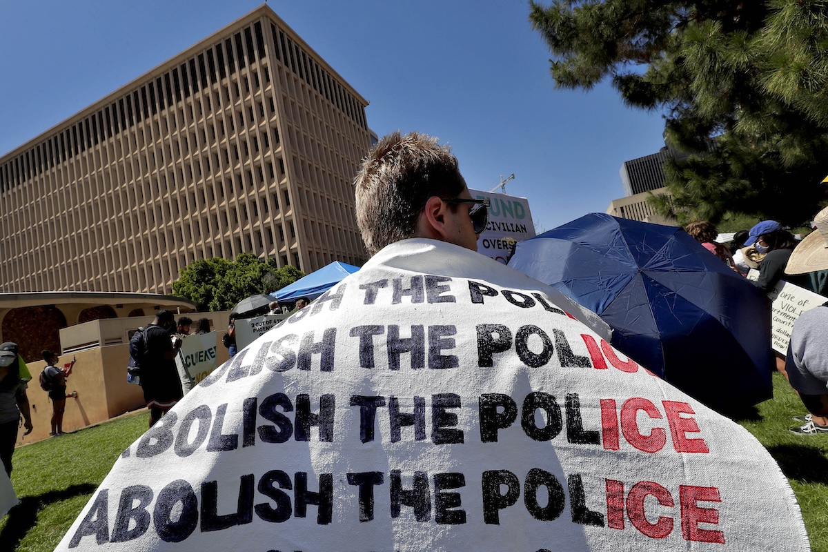 Un manifestante con uno striscione sulle spalle con scritto "Abolish the police"
