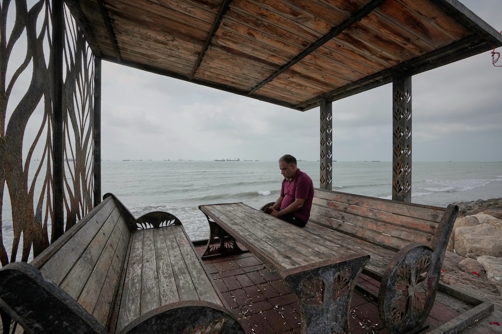 Un uomo seduto su una panchina sul lungomare, davanti allo Stretto di Hormuz (AP Photo/Vahid Salemi)