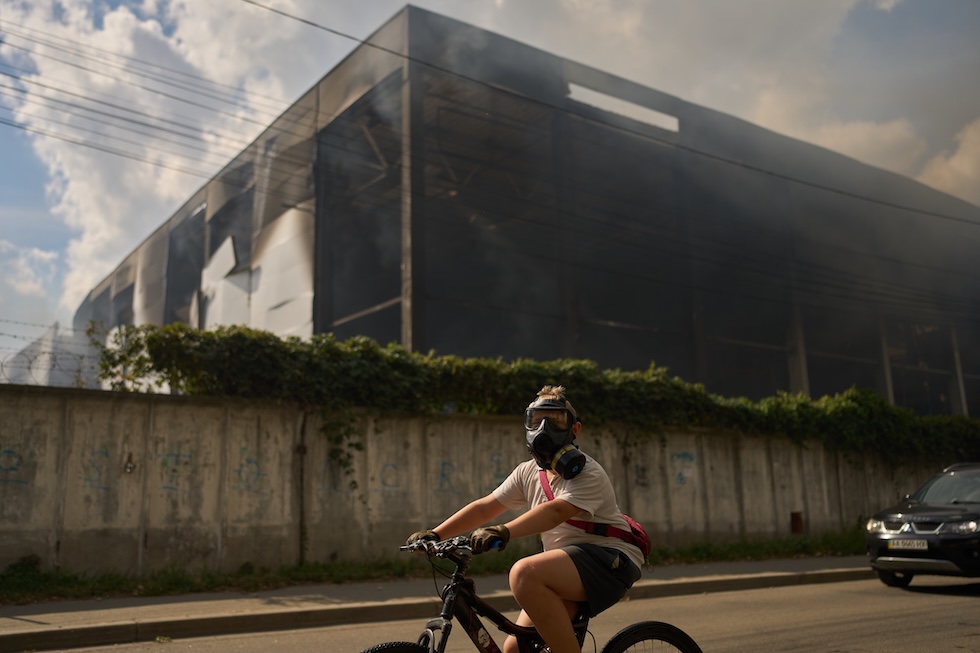 Un ragazzino passa in bicicletta davanti a un magazzino parzialmente distrutto da un bombardamento russo indossando una maschera antigas (AP Photo/Francisco Seco)