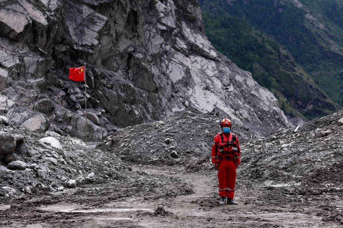 Un soccorritore vicino a una bandiera della Cina nell’area più colpita dall’esondazione tra Nepal e Tibet del 26 agosto, nella regione autonoma del Tibet (Tingshu Wang/AP)