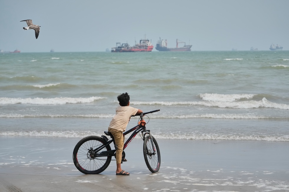 Un bambino in bicicletta in spiaggia, mentre guarda le navi commerciali nello stretto di Hormuz (AP Photo/Vahid Salemi)