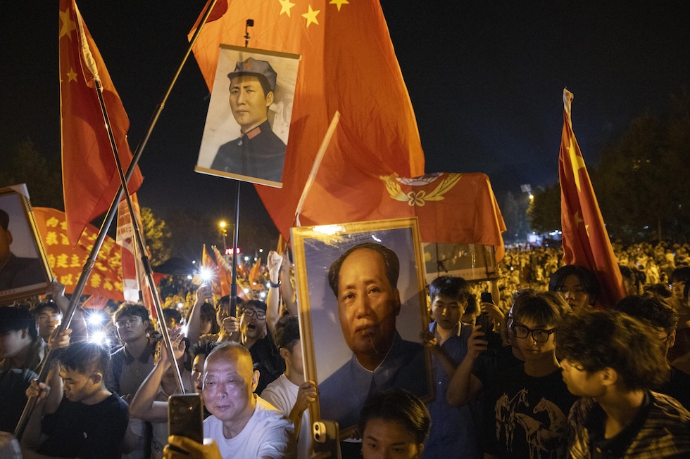 Persone tengono in mano bandiere cinesi e ritratti di Mao Zedong durante le commemorazioni per il 50esimo anniversario della sua morte, in piazza Mao Zedong, nella sua città natale (EPA/ANDRES MARTINEZ CASARES via Ansa)
