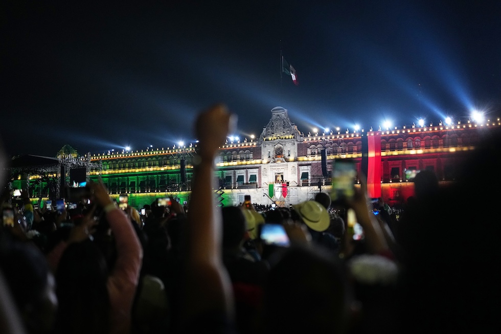 La folla allo Zócalo, la piazza principale della città, guarda la presidente del Messico Claudia Sheinbaum sul balcone del Palazzo Nazionale mentre pronuncia il tradizionale Grito de Dolores, dando il via alle celebrazioni per il giorno dell’Indipendenza (AP Photo/Eduardo Verdugo)
