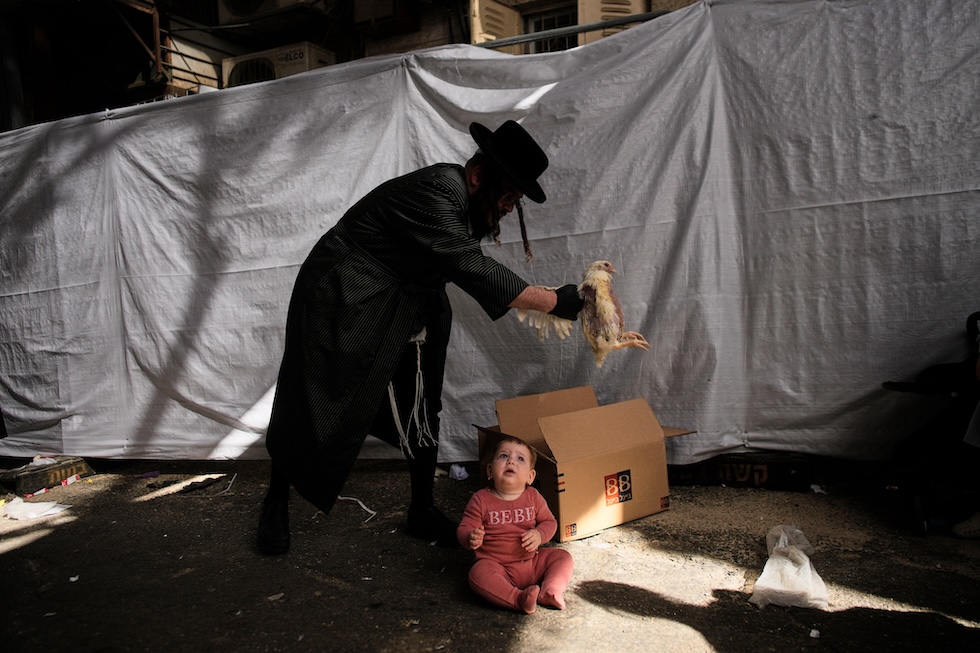 Un ebreo ultraortodosso fa girare un pollo sopra la testa del figlio durante il rito del Kaparot, il giorno dell’Espiazione, che precede lo Yom Kippur, una delle principali festività ebraiche (AP Photo/Ohad Zwigenberg)
