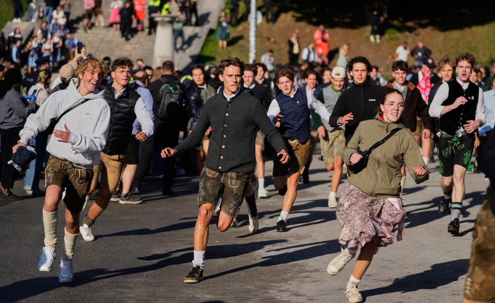 Un gruppo di persone corre verso l'ingresso dell'Oktoberfest (Matthias Schrader/AP)
