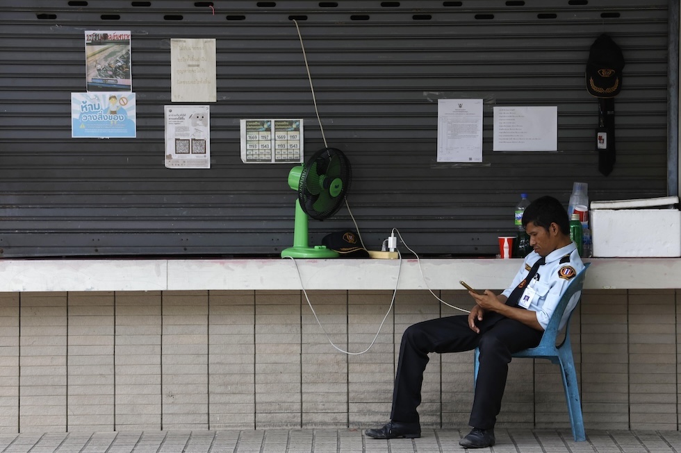 Un adetto alla sicurezza vicino a un ventilatore, mentre guarda il cellulare in un parco (EPA/RUNGROJ YONGRIT/ansa)