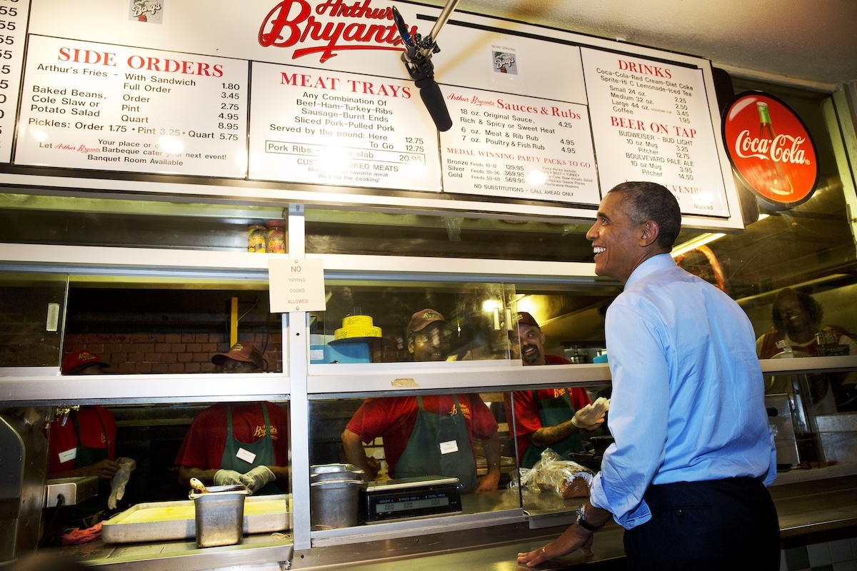 Barack Obama sorride al bancone mentre guarda i menu in alto