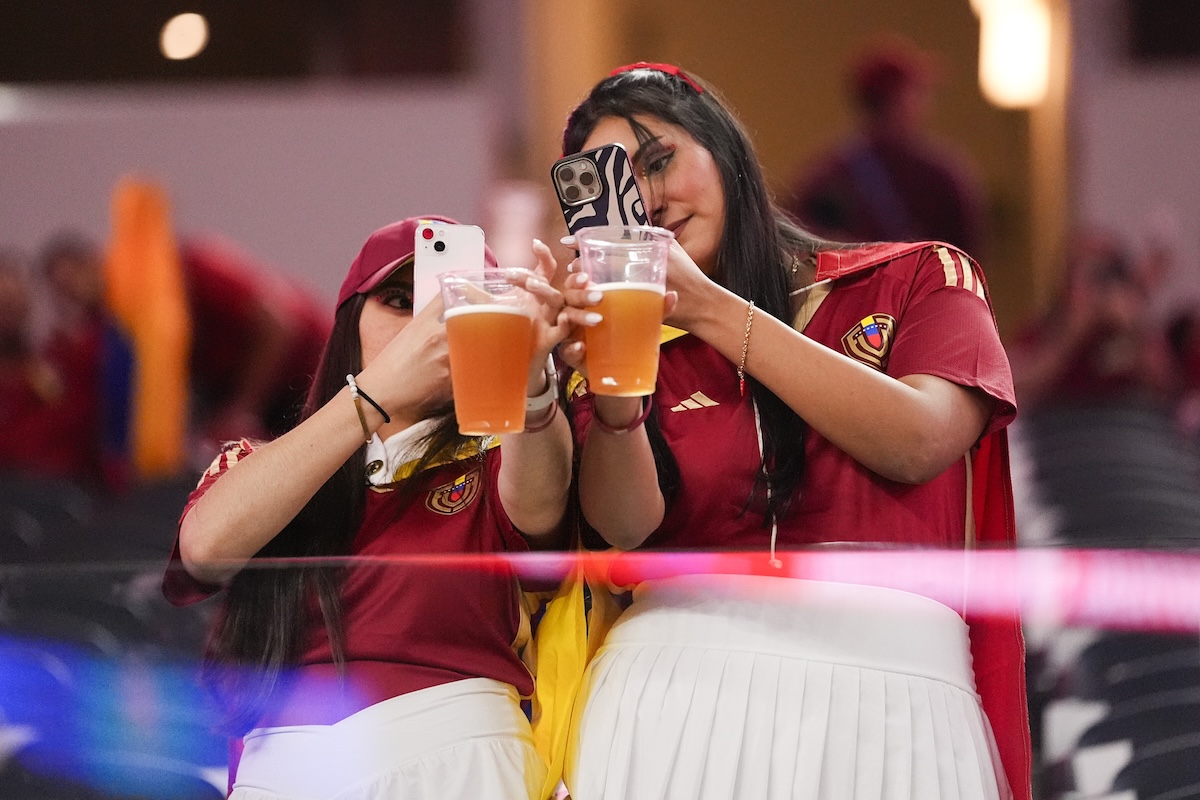 Due tifose venezuelane con un bicchiere di birra in mano e lo smartphone nell’altra