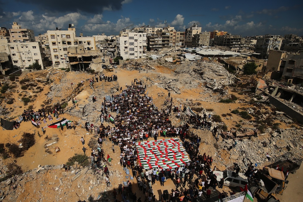 Persone riunite per un funerale attorno alle salme, avvolte nelle bandiere palestinesi, delle persone uccise negli attacchi israeliani e recuperate dalle macerie (AP Photo/Yousef Al Zanoun)