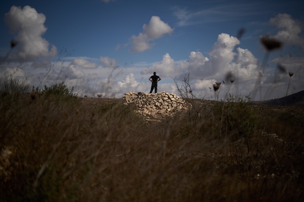 Un uomo palestinese controlla che non arrivino coloni israeliani mentre partecipa a un’iniziativa comunitaria per ripulire l’area intorno agli ulivi in vista della prossima stagione della raccolta (AP Photo/Leo Correa)
