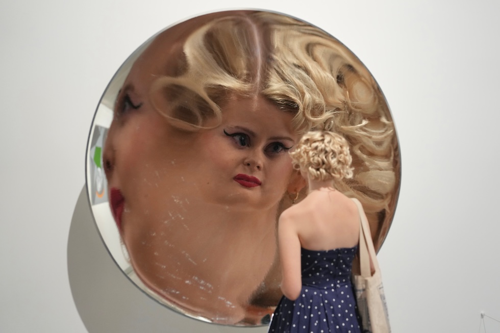 L'immagine di una visitatrice riflessa nell'installazione dell'artista gallese Cerith Wyn Evans Inverse Reverse Perverse durante l'anteprima media della mostra "The 90s: Art and Fashion exhibition" alla Tate Britain (AP Photo/Kin Cheung)