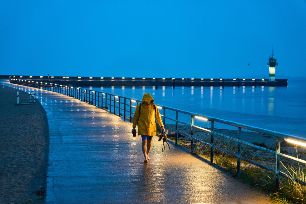 Un uomo cammina sul molo al porto di Travemeunde, con un faro sullo sfondo (AP Photo/Michael Probst)