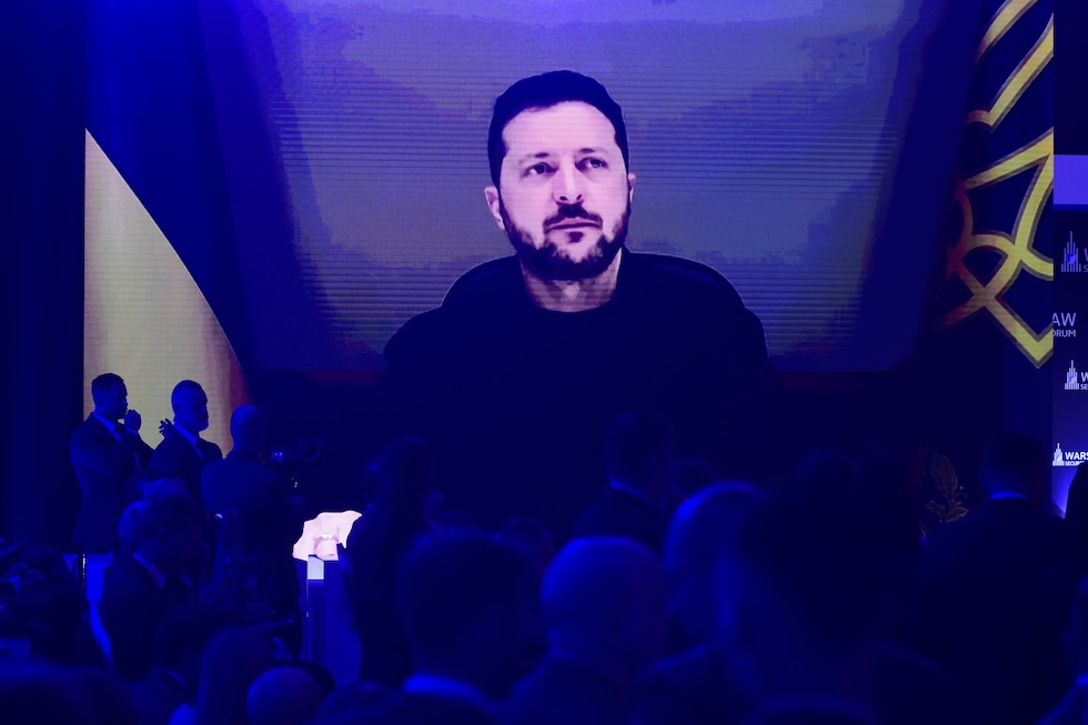 Alcune persone guardano il presidente ucraino Volodymyr Zelensky su un grande schermo durante un collegamento al Forum sulla Sicurezza di Varsavia (AP Photo/Attila Husejnow)
